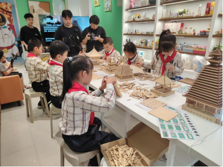 配图2：非遗文创研发中心的学生在指导孩子们拼装侗族木构.png